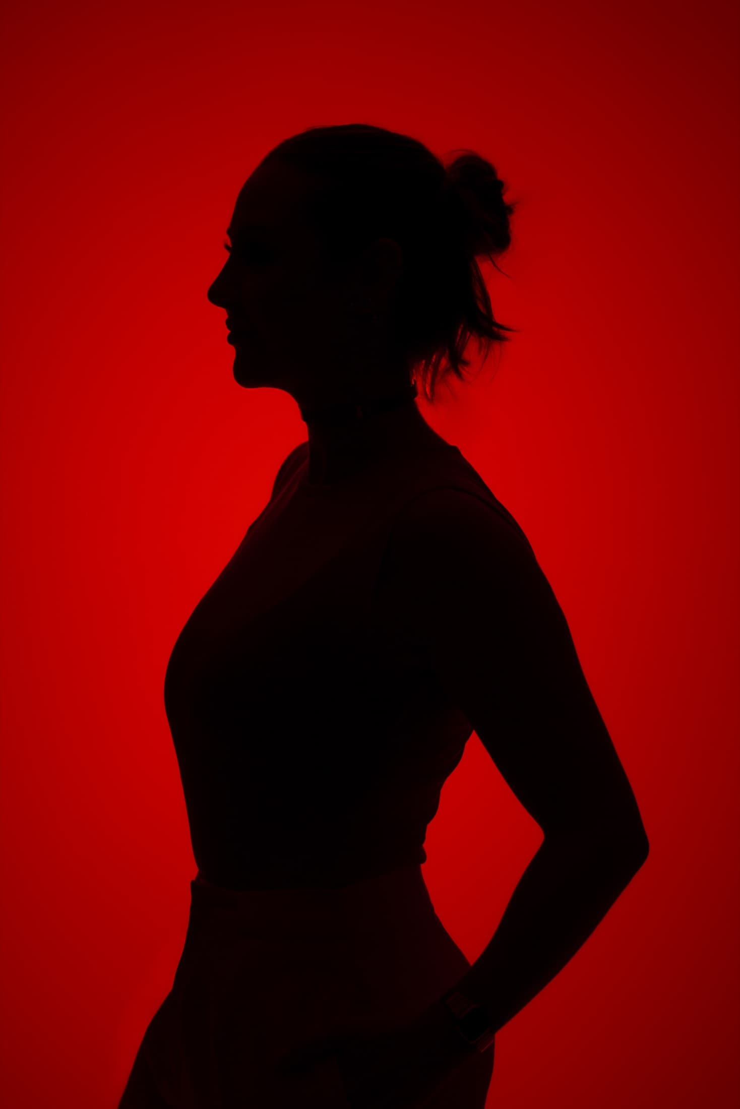 Silhueta da Dra. Ana Purr de perfil, em contraluz total contra um fundo vermelho