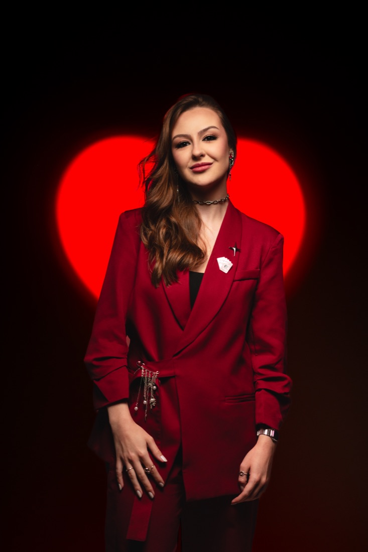Dra. Ana Purr de terno bordô diante de um coração vermelho iluminado
